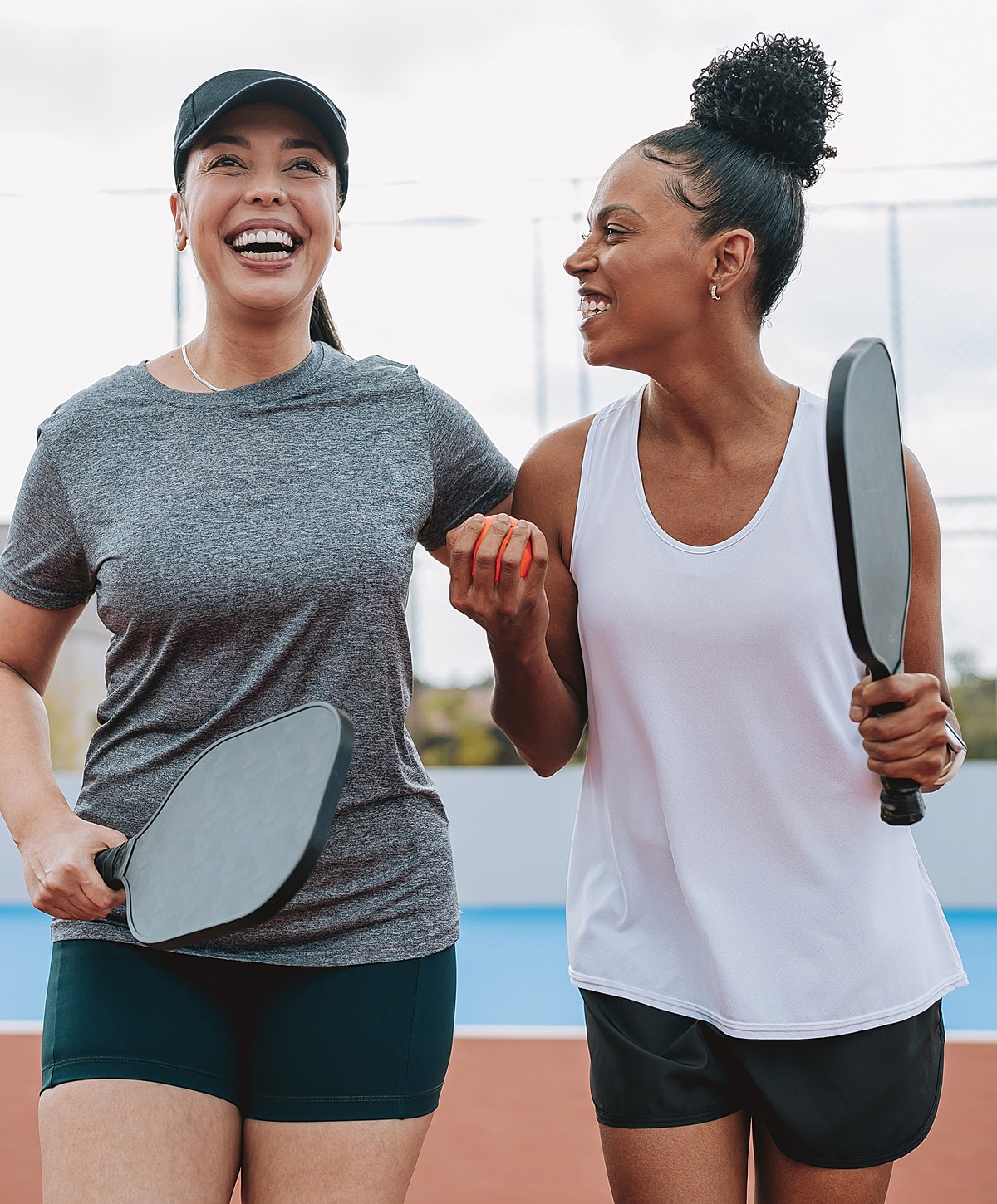 Two women smiling with pickleball paddles.