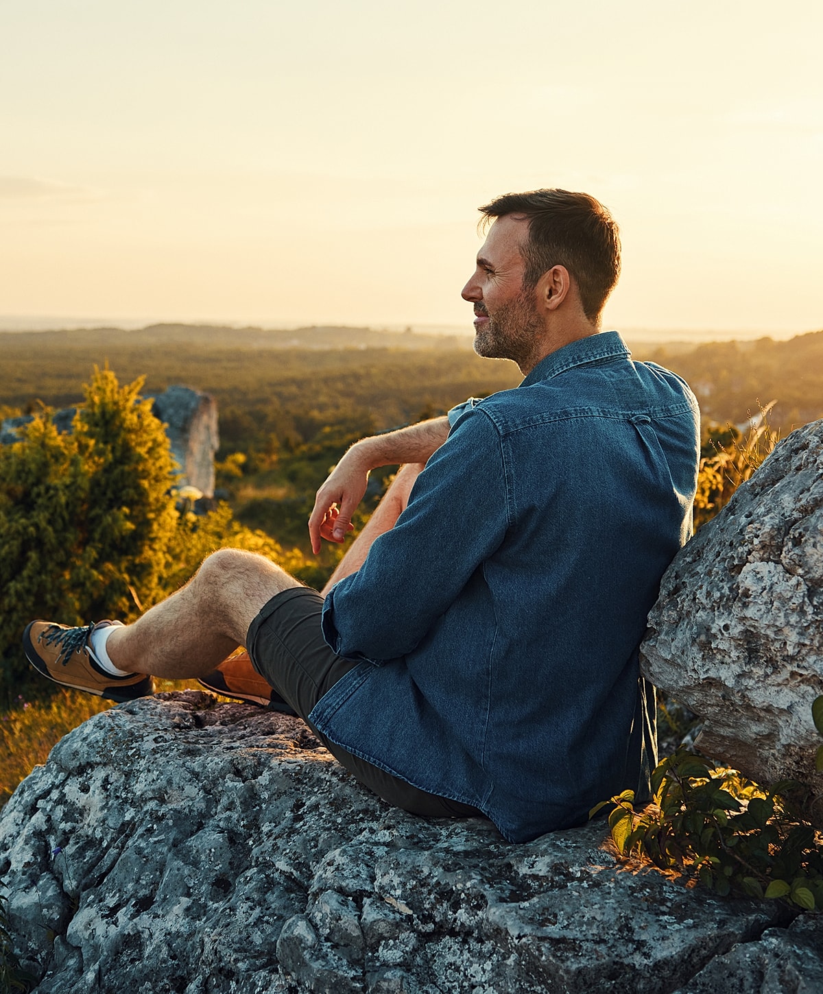 Man sitting on rock, enjoying sunset view.