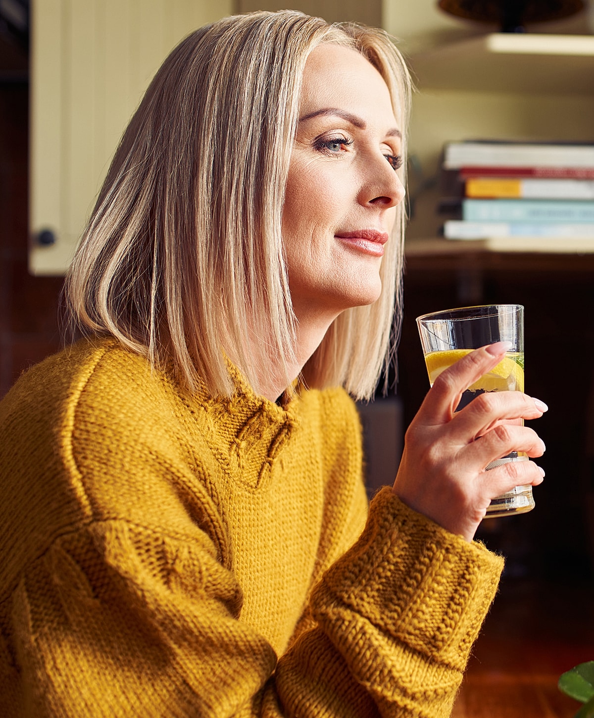 Woman in yellow sweater holding a drink.