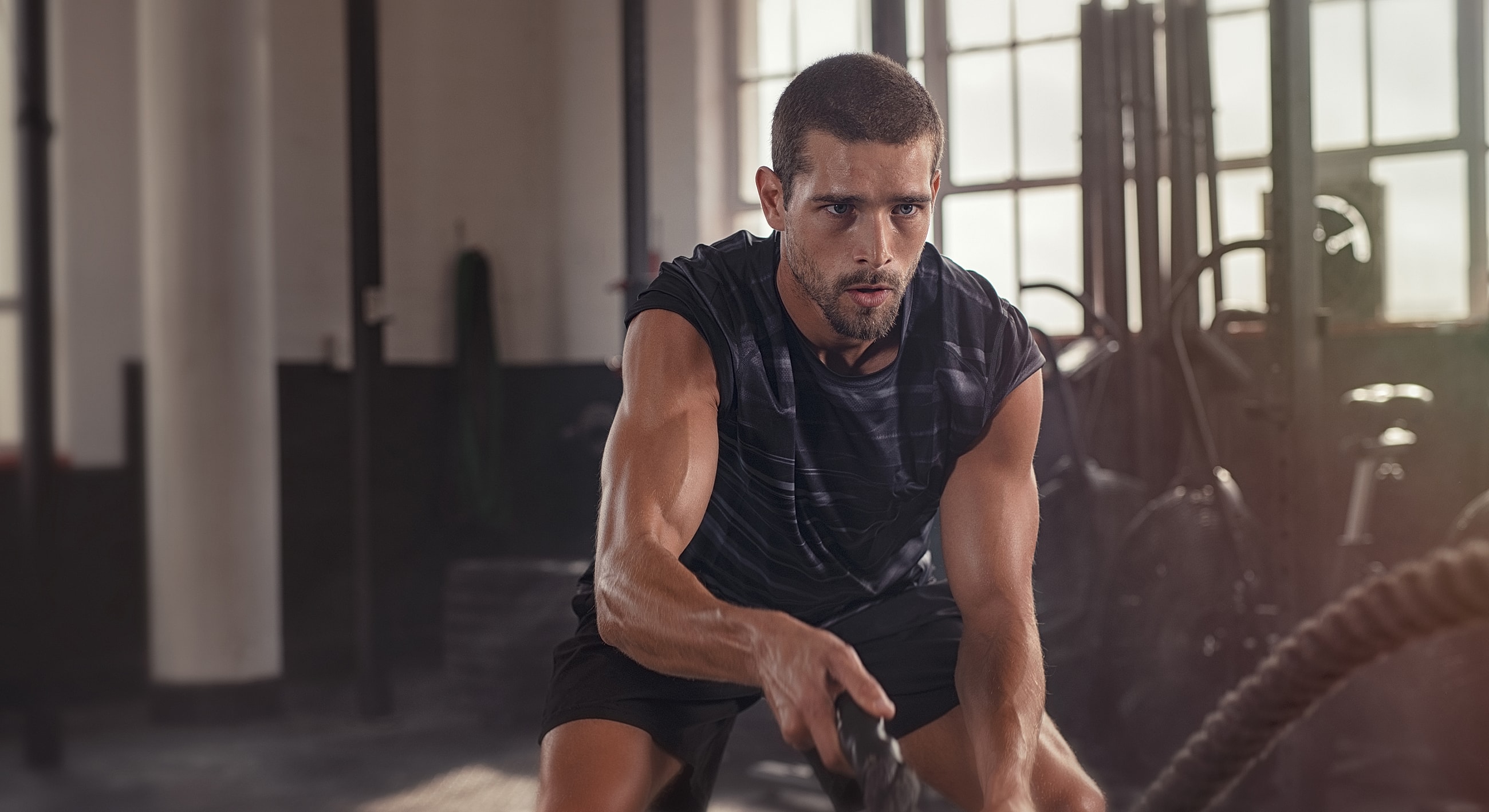 Man exercising with battle ropes in gym.