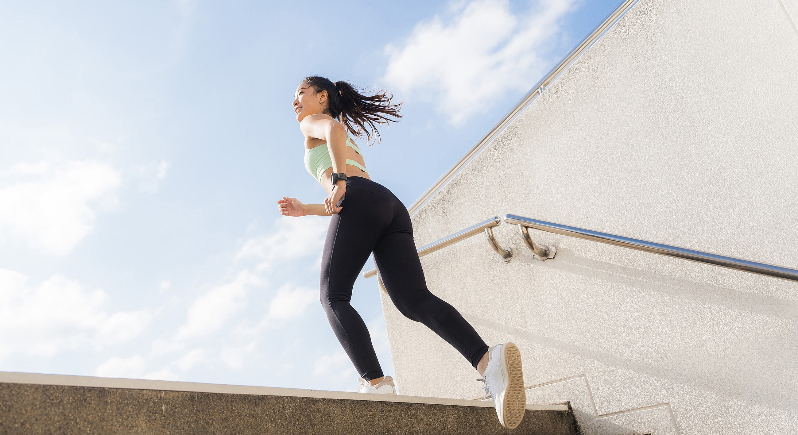 Woman jogging up stairs against blue sky.
