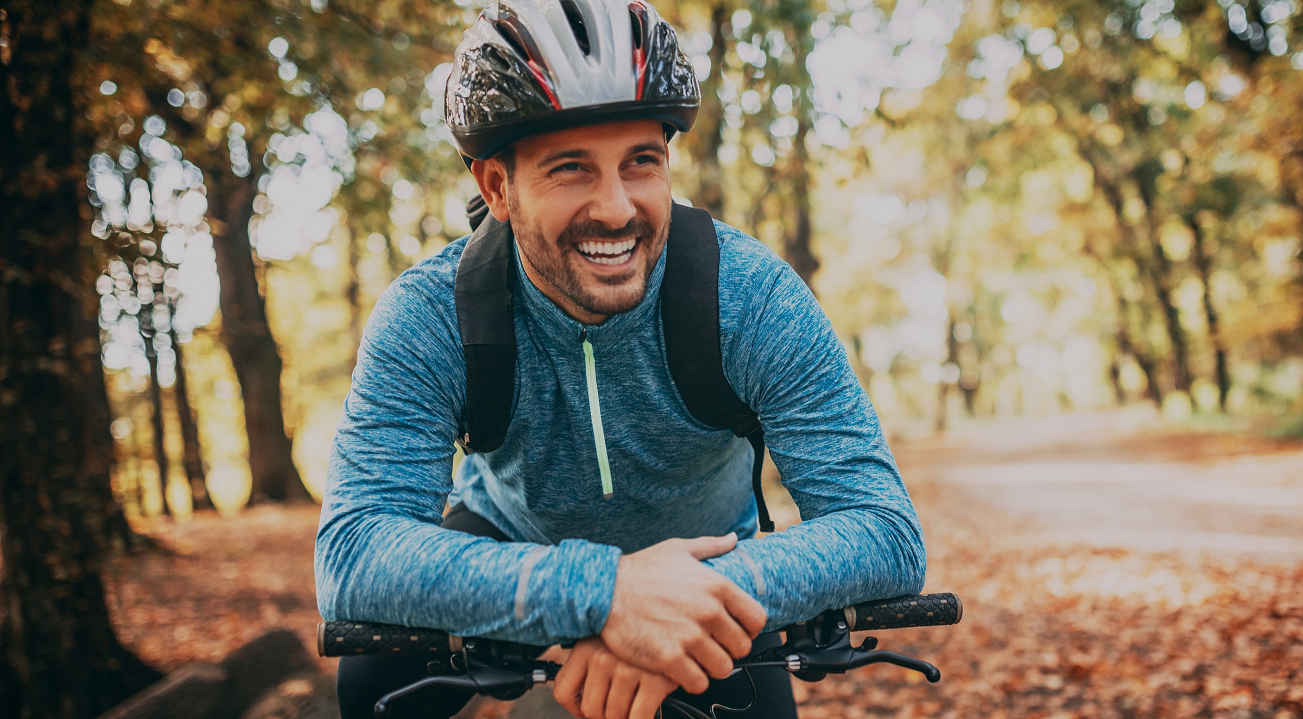 Smiling man in helmet biking through autumn forest.