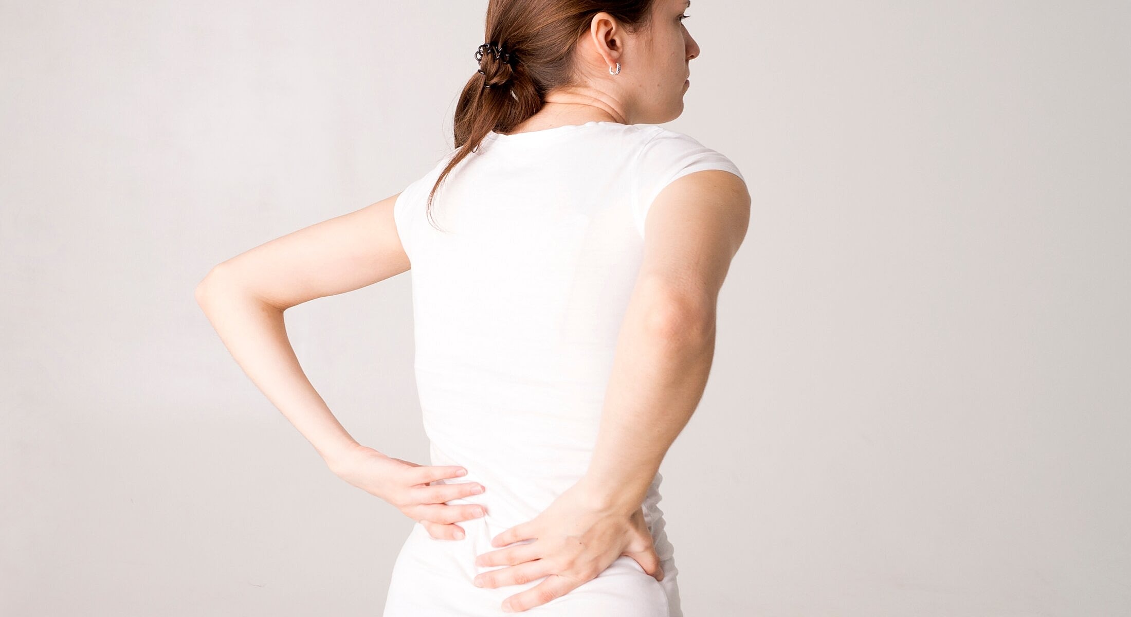 Woman experiencing back pain in white shirt.